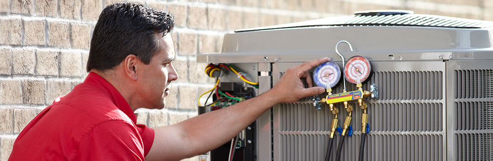 Air Conditioner Maintenance HVAC technician in red shirt checks gauges on air conditioner.