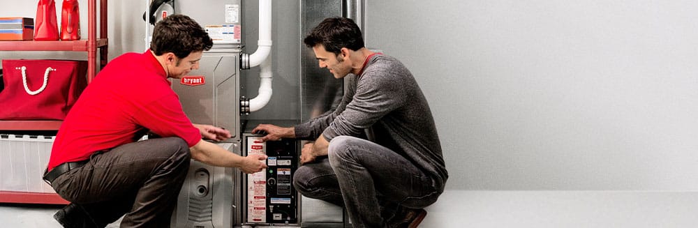 Heating technician in red shirt shows furnace to homeowner.
